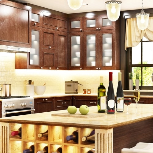 Lit wooden kitchen with wine bottles on top and on side of rack on side of island and window on right