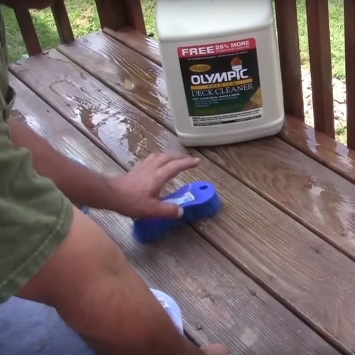 Person cleaning and scrubbing a deck with Olympic deck cleaner product