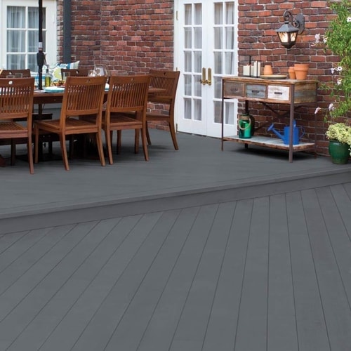 Outdoor patio area with gray wooden floor, dark wooden table set near brick wall and white-framed screen door