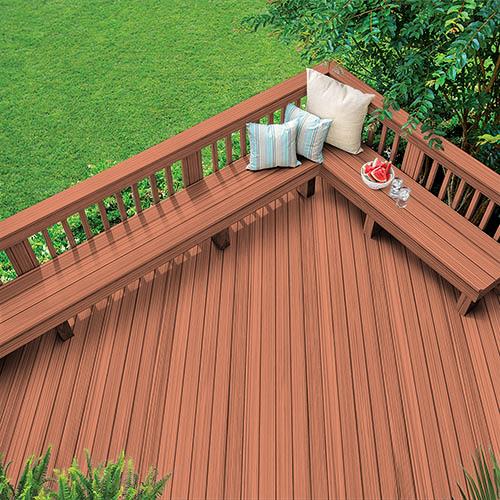 Outdoor dark brown wooden deck with bench and colored pillows around grass and trees